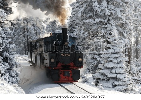 A steam train with visible water tanks rides through a winter wonderland in the German Harz mountain range