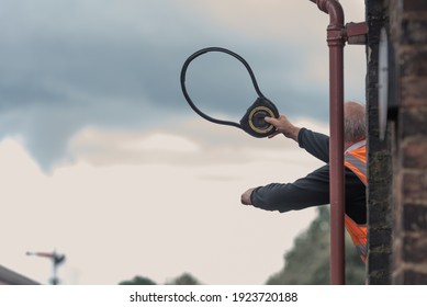 Steam Train Worker Hanging Out Of The Signal Box Waving The Token To Hand Over To The On Coming Train Driver At Goathland, UK. Orange High Viz And White Cloudy Sky. Taken In Goathland On 9 Aug 2018