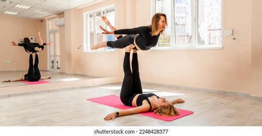 Steam yoga of two women doing yoga indoors. One woman holding the other with her arms and legs - Shutterstock ID 2248428377