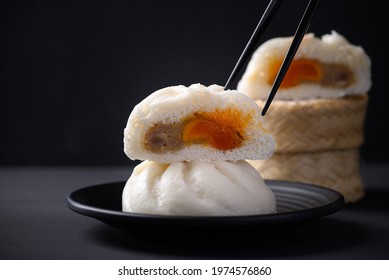 Steamed bun stuffed with minced pork and salted egg yolk eating by chopsticks on black background, Asian food