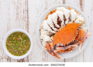 steamed crabs with spicy dipping sauce in white ceramic plate on white old wood texture background with copy space for text, top view, blue swimming crab, flower crab, blue crab