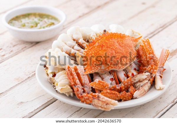 steamed crabs with spicy dipping sauce in white\
ceramic plate on white old wood texture background, blue swimming\
crab, flower crab, blue\
crab