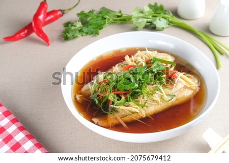 Steamed Dory fillet fish with spicy soy sauce and ginger served on white plate. Chinese food style.