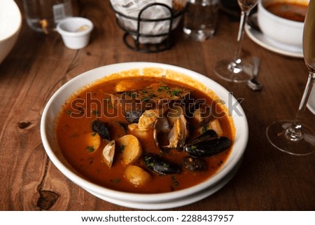 Steamed mussels in white plate with tomatoes, potatoes and bread, garnished with garlic in a restaurant setting