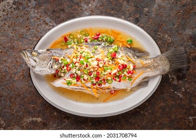 Steamed Sea Bass Fish With Lemon, Garlic, Chili And Carrot In Oval Ceramic Plate On Rusty Texture Background, Top View, Seabass, Giant Sea Perch, Barramundi, Barra