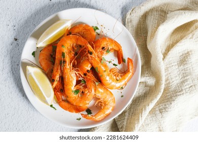 Steamed shrimps with herbs and sliced lemon on white plate. Seafood dish.