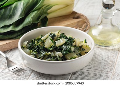 Steamed swiss chard leaves with lemon and olive oil, and fresh uncooked vegetable on background. 