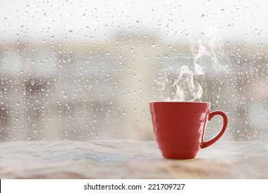 Steaming coffee cup on a rainy day window background 