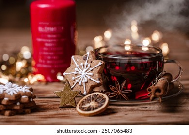 Steaming cup of red tea with gingerbread cookies, cinnamon sticks, and dried orange slices on a wooden table with a red candle and festive bokeh lights in the background. - Powered by Shutterstock