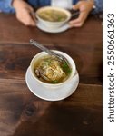 Steaming hot bowl of Soto with clear savory broth, tender shredded chicken, fresh sprouts, and a hint of lime.
