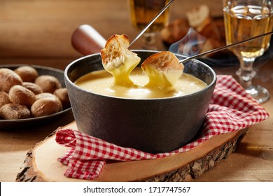 Steaming hot cheese fondue served with wine and toasted baguette on forks for dipping in close up on a rustic table
