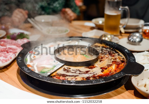 Steaming hot pot divided\
for three broths and raw ingredients to cook. Chinese cuisine and\
traditions.