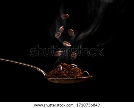 Steaming roasted coffee beans in a spoon on a black background