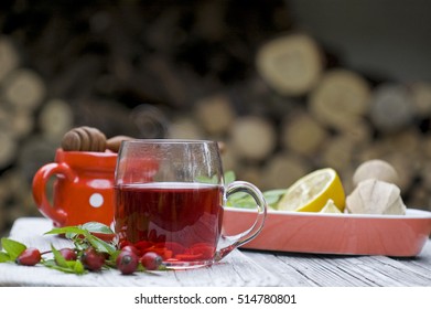 Steaming Rose Hip Tea, Rose Hip, Lemon, Honey On Rustic White Table In Exterior And Wooden Lemon Squeezer, Red, White Potted Bowl, Horizontal