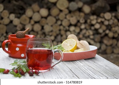 Steaming Rose Hip Tea, Rose Hip, Lemon, Honey On Rustic White Table In Exterior And Wooden Lemon Squeezer, Red, White Potted Bowl, Horizontal, Wider