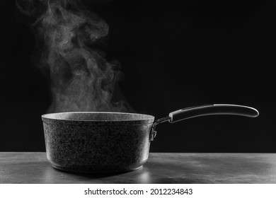 Steaming Saucepan On Grey Table Against Dark Background