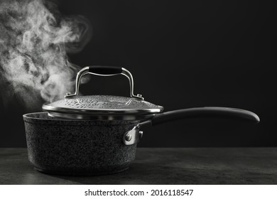 Steaming Saucepan On Grey Table Against Dark Background