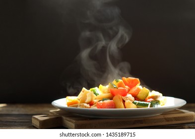 Steaming of Stir chicken with vegetables, cucumber, red bell pepper, tomato, onion and chicken. Thai dish sweet and sour sauce fried with smoke on dark background on wooden cut board.  - Powered by Shutterstock