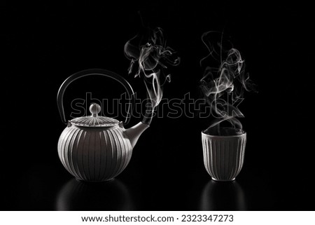 Steaming teapot and cup of tea on a dark background