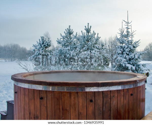 Steaming wooden hot tub with\
spa in winder with  snow and frosty Christmas trees in background -\
Image