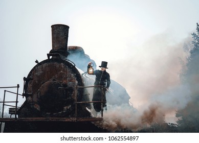 Steampunk man in a hat with a kerosene lamp in his hand stands on top of an old locomotive. Retro trip. Rusty the steam train. Fantastic locomotive of the last century.