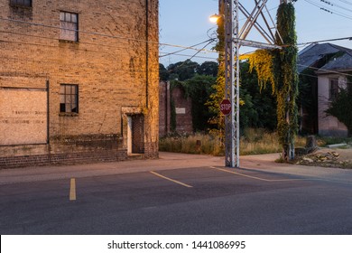 Steel Beams Supporting Power Lines Through An Alleyway Behind A Vintage Brick Warehouse In Small Rust Belt Town On Clear Evening