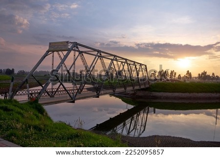 steel bridge over a river at sunset. countryside scenery. sunset by the river. rustic steel bridge over a calm river.