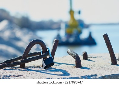 The steel cable is fixed on a reinforced concrete slab in the port. Sunny day. Simple padlock. Selective focus in the foreground. Silhouette of a ship in a strong blur. Bracing and securing concept. - Powered by Shutterstock