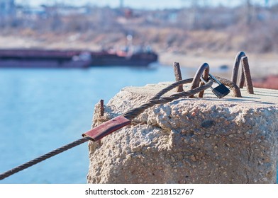 The steel cable is fixed on a reinforced concrete slab in the port. Sunny day. Simple padlock. Selective focus in the foreground. Silhouette of a ship in a strong blur. Bracing and securing concept. - Powered by Shutterstock
