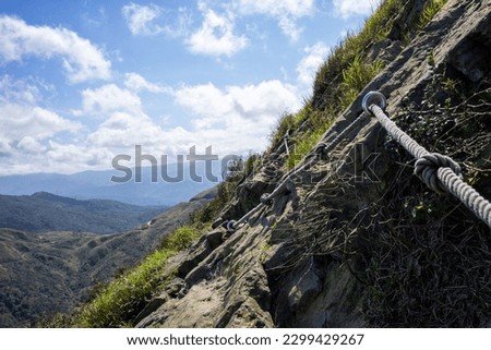 A steel cable handrail runs along the rocky peak of Teapot mountain. A dangerous hiking trail in Taiwan.