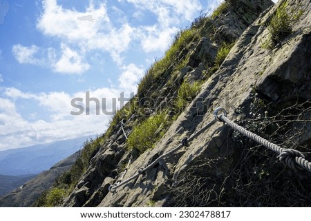 A steel cable handrail runs along the rocky peak of Teapot mountain. A dangerous hiking trail in Taiwan.