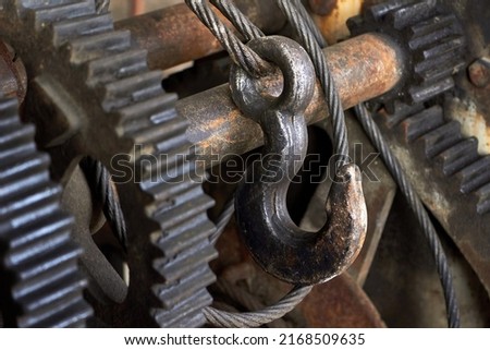 Steel cable sling hoist hook with gears. Wire rope sling and crawler drum of lifting crane machine. Closeup selective focus industrial mechanism detailing steampunk background.