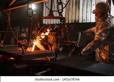 Steel casting process in foundry. Worker in protective suit pouring molten steel into molds.