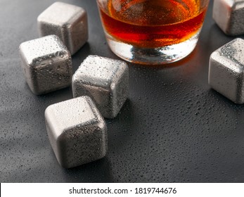 Steel cubes imitating ice. For cooling drinks. With a glass of whiskey. Covered with drops. Close-up.