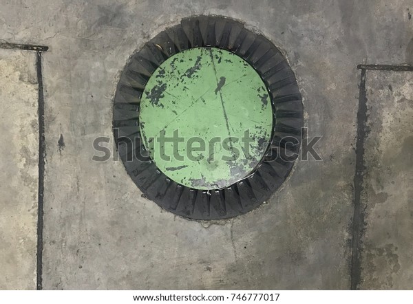 Steel cylinder or Iron metal green cover on\
concrete ground. It is steel used for closing holes on concrete\
floors that are in place for oil refilling or gas to car. It use\
protect Danger for\
traveler