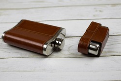 Steel Flask For Alcohol With Brown Leather Lies With An Open Lid On A White Wooden Table