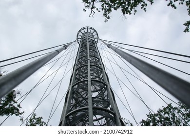 Steel gray construction of a high lookout tower in Brno, Czech Republic, bottom view into the clouds. There are deciduous trees around the view.