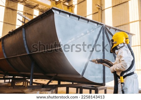 Steel Grit blasting process, Industial worker using steel grit blasting process preparation cleaning surface on steel structure before painting in factory workshop.