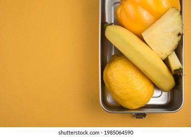 Steel Lunchbox With Yellow Fruits And Vegetables On A Yellow Background. Top View. Space For Text