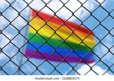 A steel mesh against the background of a blue sky and a flagpole with flag of lgbt pride - Shutterstock ID 2168803175