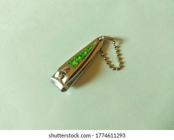 Steel Nail Clipper Isolated On Mint Color Background. Green Design On Top And Ball Chain For Hang.