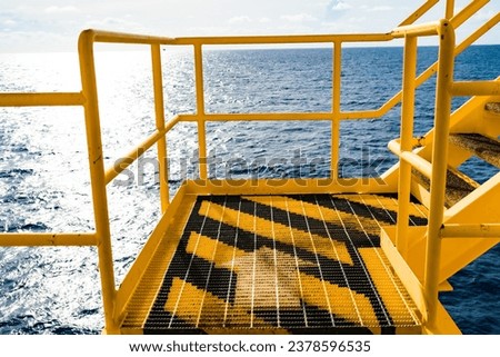 Steel netting creates walkways on oil and gas drilling platforms, painted white and yellow and with arrows to guide the walkways.