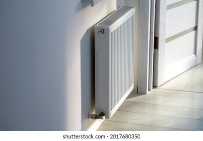 A steel panel heating radiator is placed under the windowsill on a white wall. Selective focus.