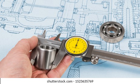 Steel Part Measurement By Caliper In Human Hand. Ball Bearing On Technical Drawing Of Combustion Engine. Quality Control. Engineer When Measuring A Metal Roller Diameter By Precise Tool. Project Plan.