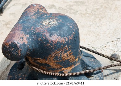 The Steel Rope Of The Ship Is Fixed On An Old Rusty Cast-iron Bollard. Fragment Of The River Pier. Close Up. No People.