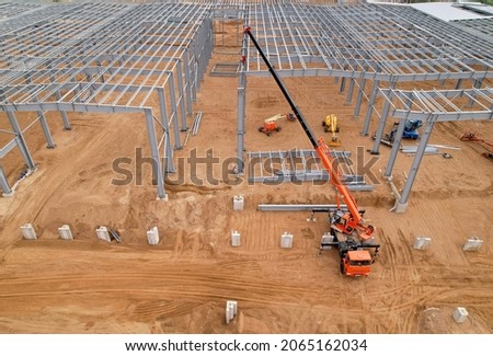 Steel Structure Warehouse Building. Industrial Building on light gauge steel framing. Frame of modern hangar or factory. Truck crane on construction site during assembling metal structure.