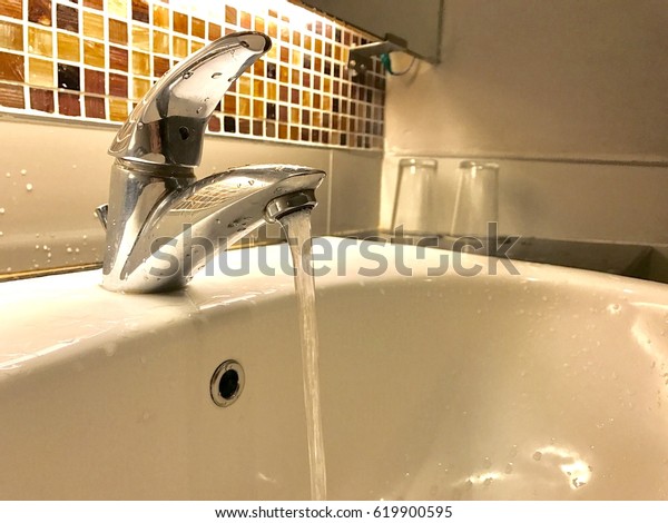 steel water tap with running water and sink in\
a bathroom with brown mozaic marble and two of transparent glass as\
decoration