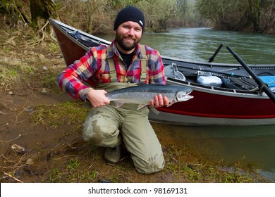 A steelhead fisherman holds his trophy fish by his boat and the river in Oregon.