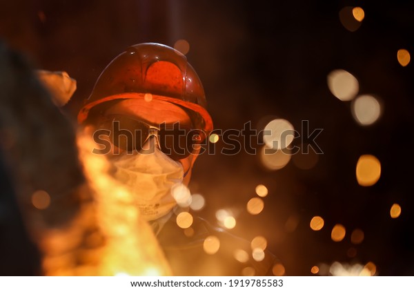 A steelmaker pours pig iron from a\
blast furnace, sparks and splashes of hot metal\
fly.