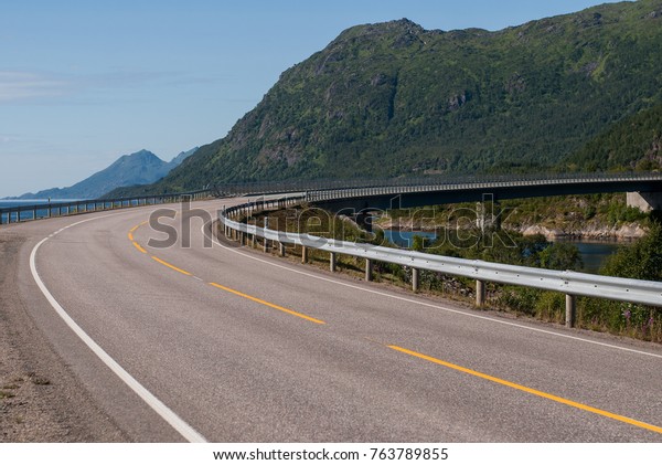 A steep curve of the road against the backdrop\
of mountains